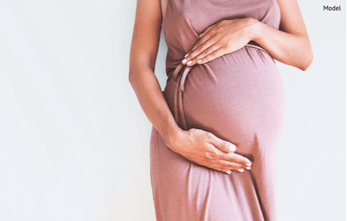 Pregnant woman in dress holds hands on belly