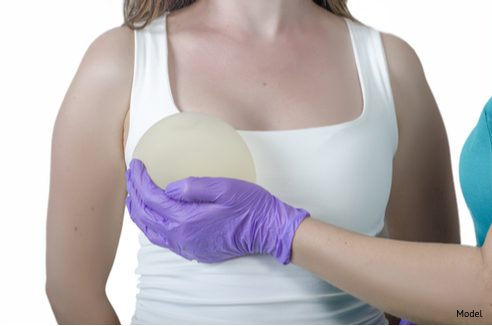 Surgeon holding a round silicone implant in front of a womans breast-img-blog