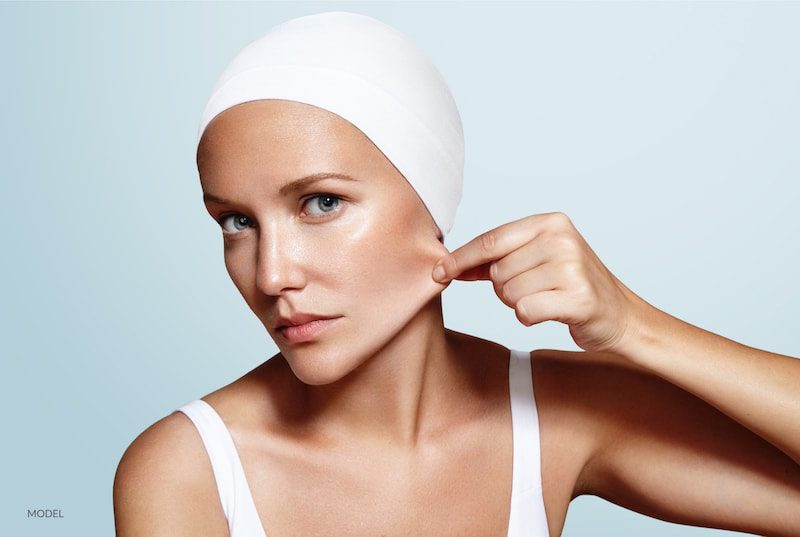 Young woman pulling facial skin back on lower face. Skin tightening concept.