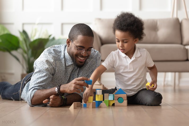 Father and son play with blocks on the hardwood floor.