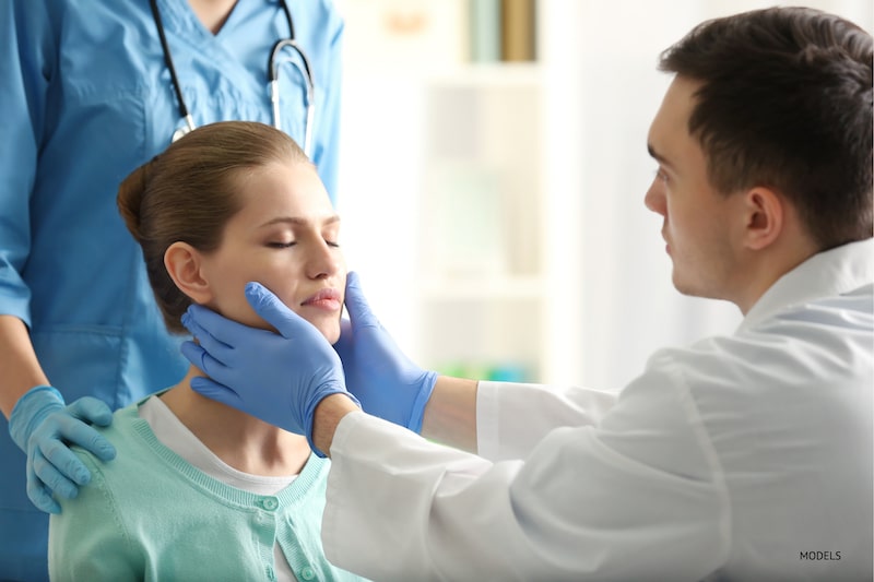 Médico colocando as mãos na mandíbula de uma paciente do sexo feminino
