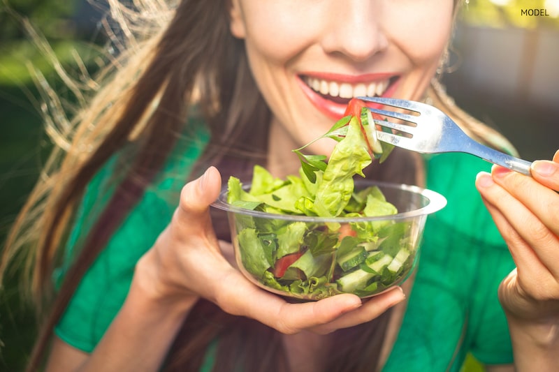 Happy woman eating a green salad and smiling.
