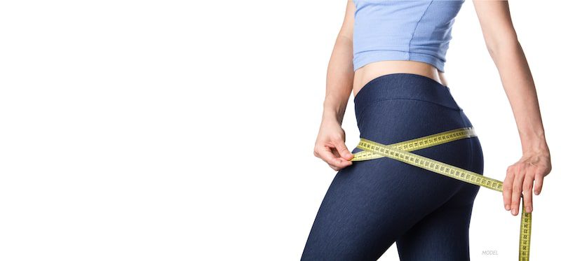 Woman wrapping a tape measure around her lower body, including her hips and buttocks,
