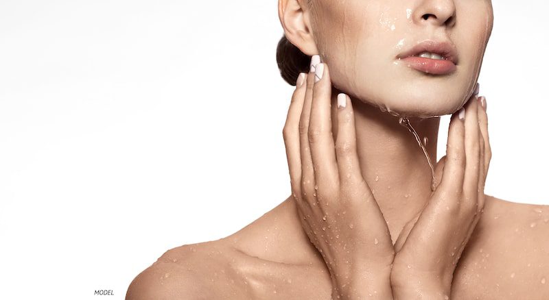 Woman splashing water on her face, close-up of her lower face.