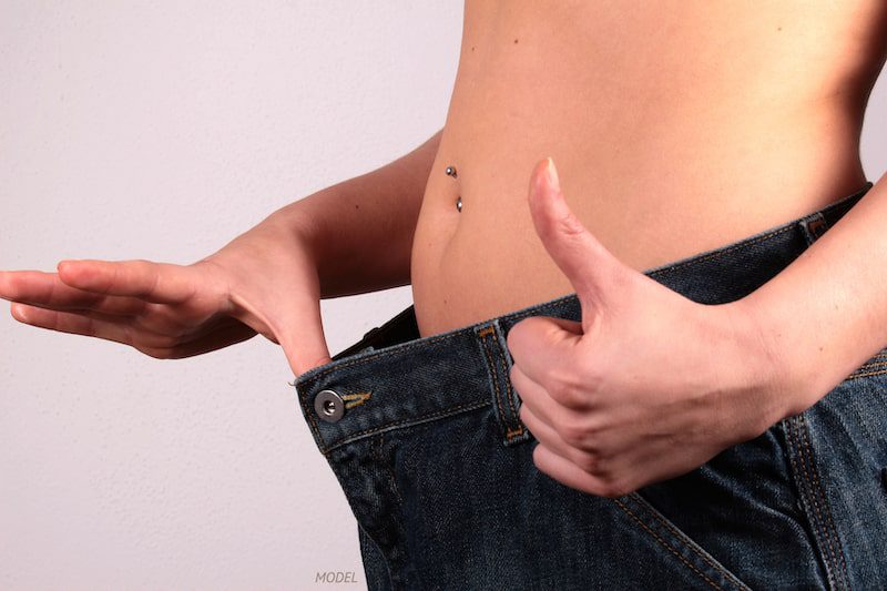 Close-up of a woman holding out too-big jeans from her newly trimmed midsection