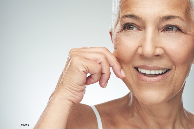 Happy aging woman pulling the skin on her cheek to show aging process.