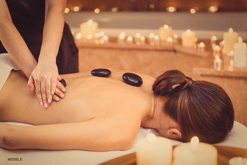 Woman undergoing hot stone massage while surrounded by candles