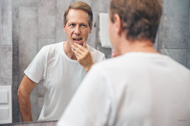 Middle-aged man studying his face in the mirror