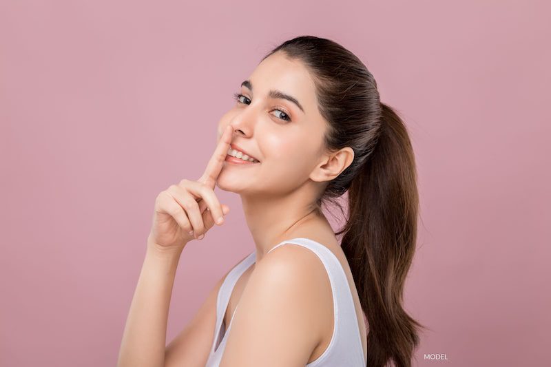 Beautiful woman who is smiling at the camera while touching her nose with her finger