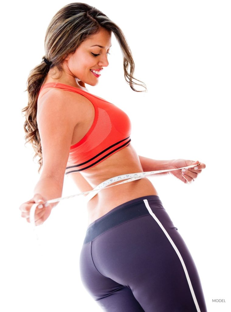 Fit woman measuring her waist in exercise clothing, looking pleased.