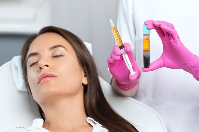 Beautiful woman lying back while a nurse holds a syringe filled with PRP