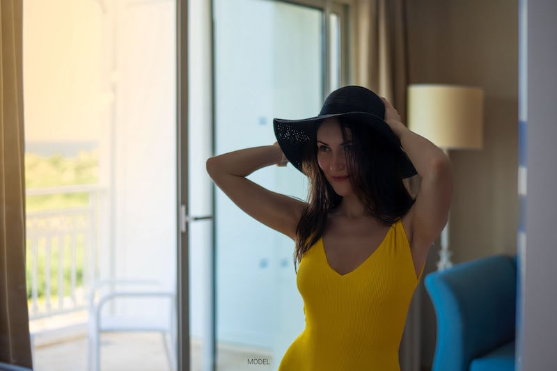 Woman looking in a mirror, wearing a yellow shirt and black hat.