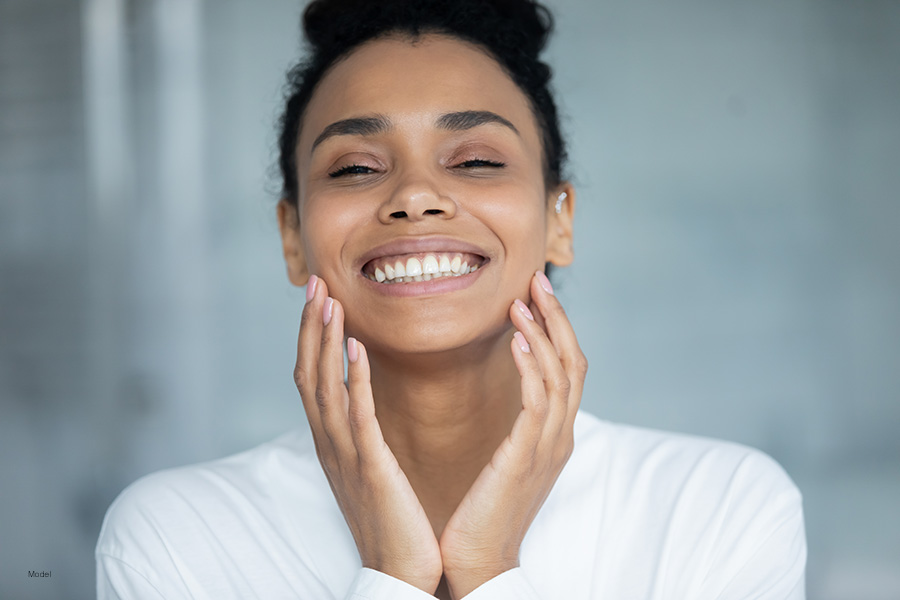 Beautiful woman smiling as she touches her hands to her smooth facial skin