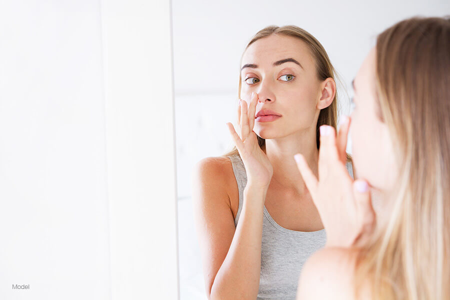 woman looking in a mirror and touching her nose as if examining it's appearance
