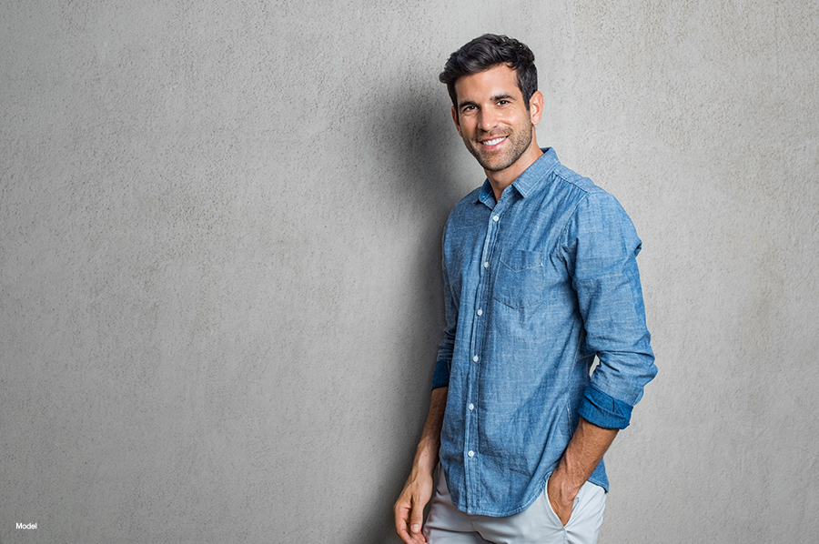 Happy smiling man leaning against grey wall. 