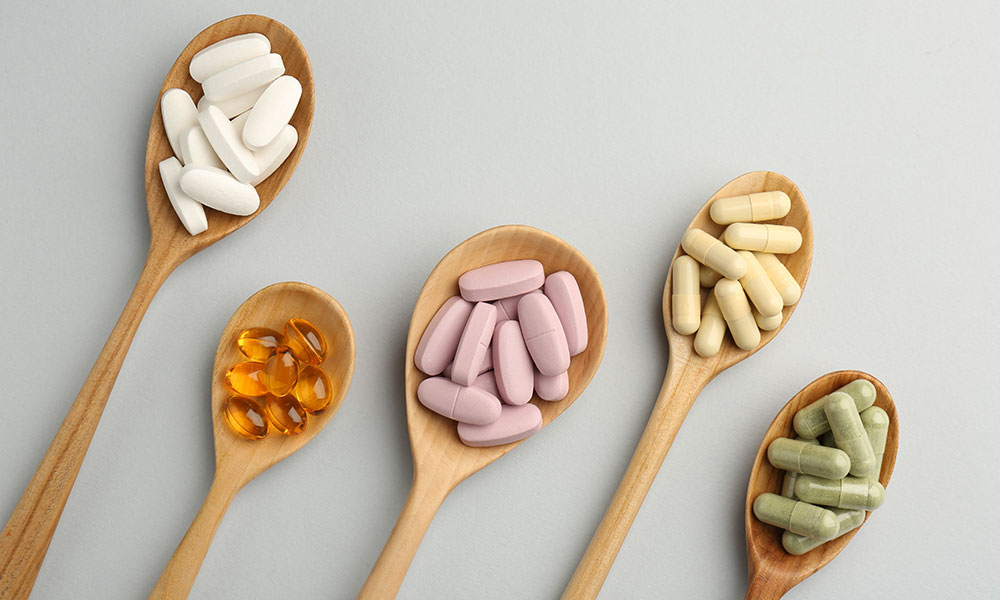 Different vitamin pills in spoons on light grey background
