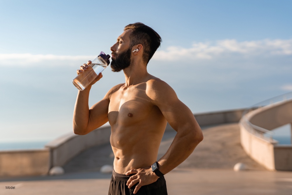 man shirtless with athletic body drinking water from bottle